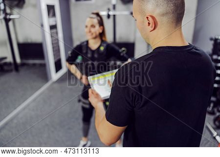Woman In A Black Ems Training Suit Standing In The Middle Of A Training Center And Part Of The Back 