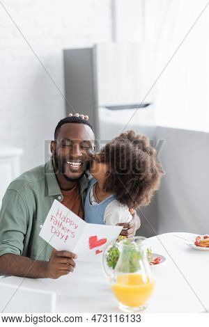 Curly African American Kid Kissing Cheek Of Happy Father With Greeting Card On Fathers Day.