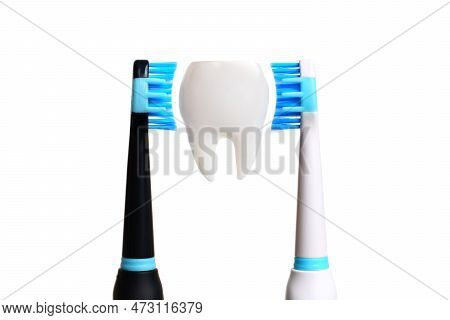 Large Tooth Model Placed Between Black And White Electric Toothbrushes On A White Background. The To