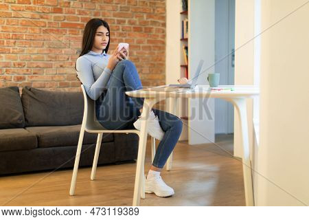 Teen Girl Sitting At Desk And Holding Smartphone, Looking At Screen, Using App Or Messaging, Living 