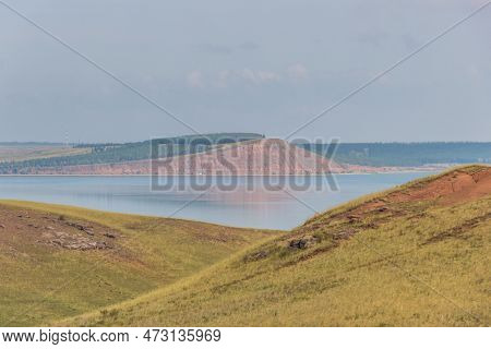 Rocky Hills And Ravine. Red Mountain On The Other Side Of The Lake