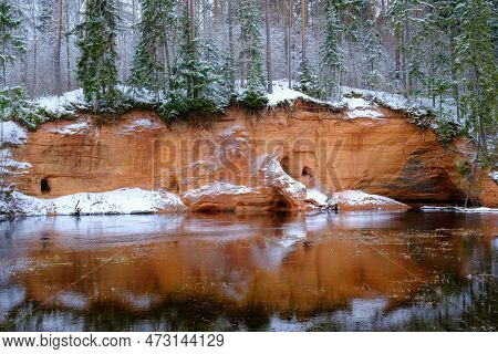 Red Sandstones On The Bank Of The River Salaca. Red Sandstone Rock In Bezdeligu Winter. Skanaiskalns
