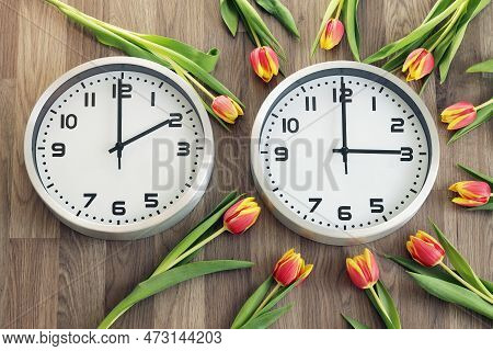Two Clocks, One Showing Two O'clock, The Other Showing Three O'clock. Tulips Around The Second One. 