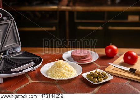 Different Ingredients For Making Pizza - Grated Cheese, Olives, Salami, Tomatoes On The Kitchen Tabl