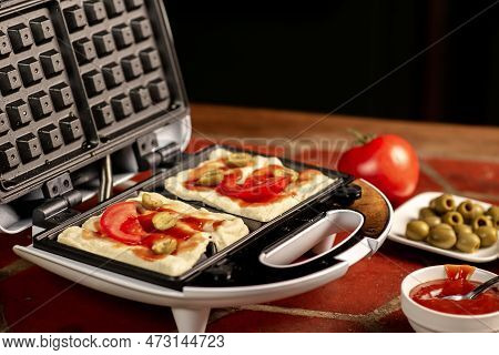 Cooking Pizza Waffle, Piffle. Waffle Iron And Different Ingredients On The Kitchen Table.