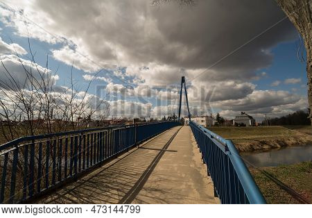 Suspension Bridge (footbridge) In Blue, Over The Kamienna River . A Footbridge Under A Blue Sky With