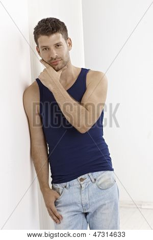 Casual joven apoyado contra la pared, vistiendo camiseta y pantalones vaqueros.