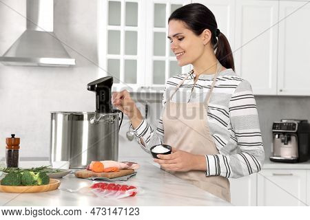 Woman Salting Products Near Pot With Sous Vide Cooker At Table In Kitchen. Thermal Immersion Circula