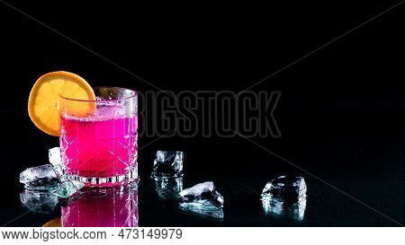 A Bright Glowing Dragonfruit Cocktail With Ice Against A Black Background.