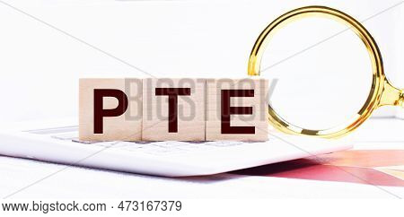 Three Wooden Cubes With The Text Pte Pearson Test Of English Stand On A White Calculator Near A Magn