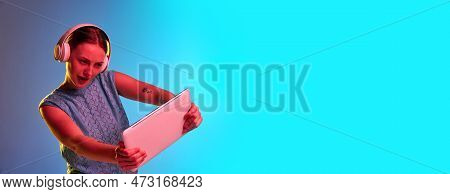 Portrait Of Gamer Young Girl Wearing Headphones, Holding Tablet With Excited Face Over Blue Backgrou