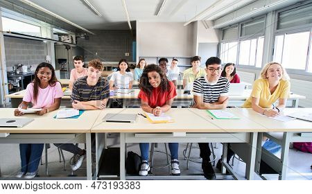 Smiling Group Of University College Sitting At Classroom Looking At Camera. Portrait Of Cheerful Stu