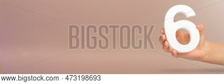 Number Six In Hand. A Hand Holds A White Number 6 On A Red Background With Copy Space. Concept With 