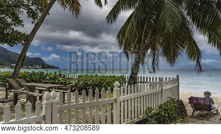 A Relaxation Area On A Tropical Beach Behind A White Wooden Fence. A Table And Benches Are Visible. 