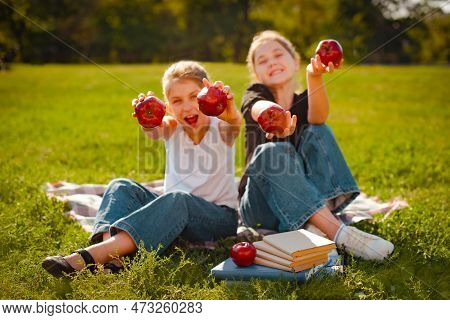 Classmates Girls Play With Red Apples On Green Grass In Park. Focus On Hands With Apple