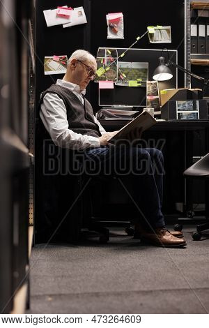 Senior Private Detective Reading Legal Documents In Arhive Room, Working Overhours At Criminal Case.