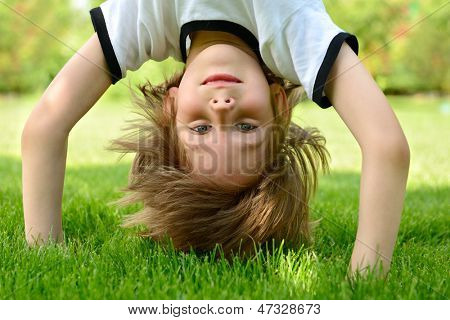 Glücklich kleiner Junge stehen kopfüber auf grünem Gras im Frühlingspark