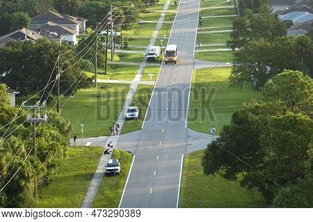 Aerial View Of American Yellow School Bus Picking Up Children At Sidewalk Bus Stop For Their Lessong