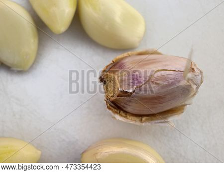 Garlic Clove Unpeeled Combined With Peeled Ones On A White Cutting Board