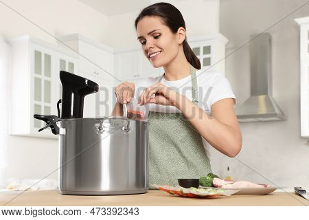 Woman Putting Vacuum Packed Salmon Into Pot With Sous Vide Cooker In Kitchen. Thermal Immersion Circ