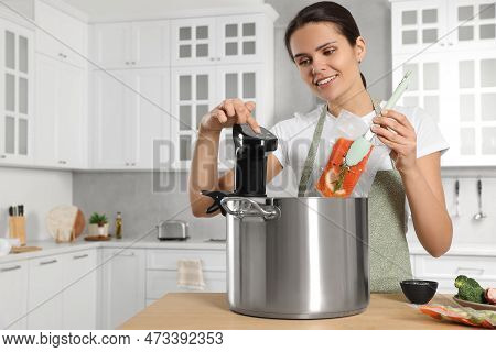 Woman Putting Vacuum Packed Salmon Into Pot And Using Thermal Immersion Circulator At Table In Kitch