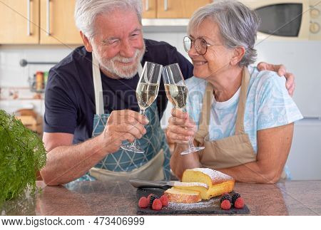Beautiful Senior Couple In The Home Kitchen Holding Glasses Of Wine Ready To Eat Their Homemade Plum