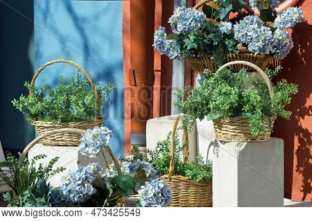 Wicker Baskets With Blue Hydrangea And Other Plants On The Street