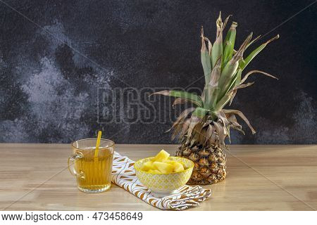 Half A Pineapple On The Table, A Yellow Bowl Full Of Pineapple Chunks And A Glass With A Straw And P