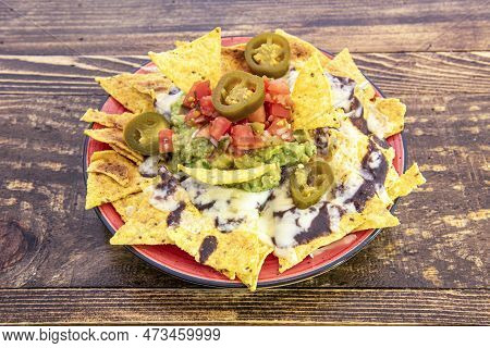 Mexican Corn Nachos With Guacamole, Beans, Chipotle, Jalapenos, Chopped Red Tomato On Red Plate And 