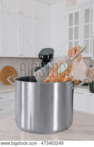 Woman Putting Vacuum Packed Meat Into Pot With Sous Vide Cooker In Kitchen, Closeup. Thermal Immersi