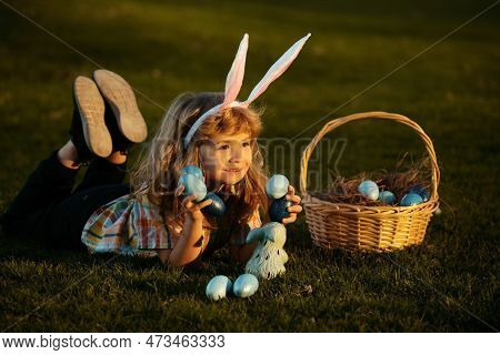 Child With Easter Eggs In Basket Outdoor. Boy Laying On Grass In Park. Easter Egg Hunt. Fynny Kids P