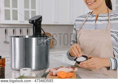 Woman Salting Meat Near Pot With Sous Vide Cooker At Table In Kitchen, Closeup. Thermal Immersion Ci