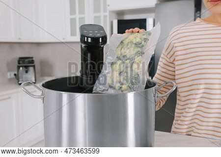 Woman Putting Vacuum Packed Broccoli Into Pot With Sous Vide Cooker In Kitchen, Closeup. Thermal Imm