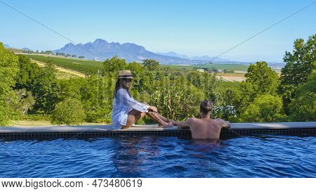 Couple In Swimming Pool Looking Out Over The Vineyards And Mountains Of Stellenbosch South Africa