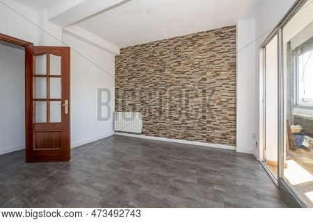 Empty Living Room With Gray Sintasol Floors, Exit To The Terrace And A Wall Covered With Stone Tiles