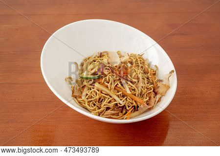 White Bowl Of Sauteed Noodles With Fresh Vegetables And Yakisoba Sauce On Orange Table