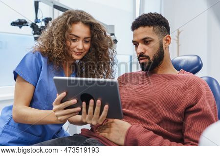 Young Woman Dentist Doing Preventive Examination To Multiracial Man, Showing Him X-ray Image In Digi