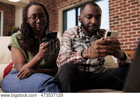 African American Couple Spending Time Looking At Social Media Content On Smartphones And Ignoring Ea