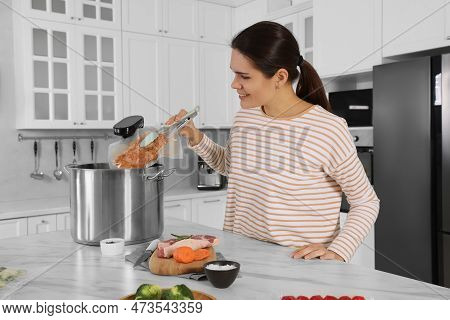 Woman Putting Vacuum Packed Meat Into Pot With Sous Vide Cooker In Kitchen. Thermal Immersion Circul
