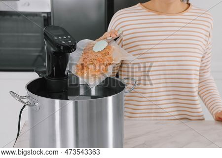 Woman Putting Vacuum Packed Meat Into Pot With Sous Vide Cooker In Kitchen, Closeup. Thermal Immersi