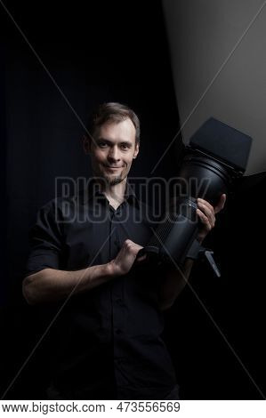 Portrait Of A Gaffer Man With A Professional Lighting Head Device In His Hands On A Black Background