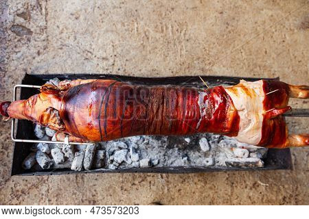 A Young Pig Is Roasted On A Spit Over Coals.
