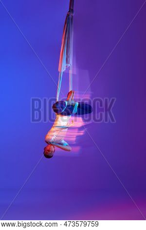 Young Man, Professional Aerial Gymnast Doing Acrobatic Tricks With Aerial Ribbon Against Gradient Bl