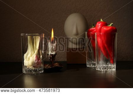 Still Life With Candlestick With Burning Candle, Red Ramiro Peppers And Garlic Bulb In The Glass Bea