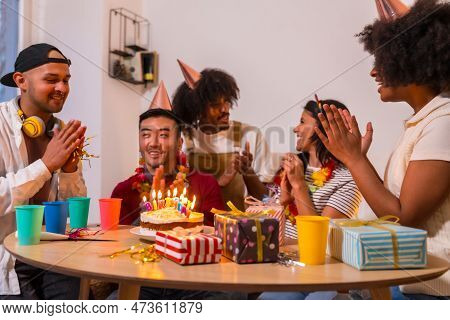 Multi-ethnic Group Of Friends At A Birthday Party On The Sofa At Home With A Cake And Gifts, Smiling