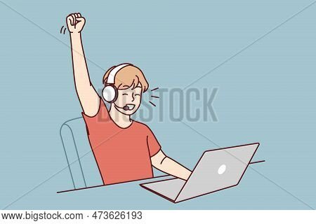 Delighted Teen Boy Sitting At Table With Laptop Playing Video Game And Defeating Virtual Opponents. 