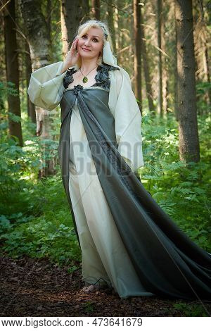 Adult Mature Woman 40-60 In A Green Long Fairy Dress In Forest. Photo Shoot In Style Of Dryad And Qu