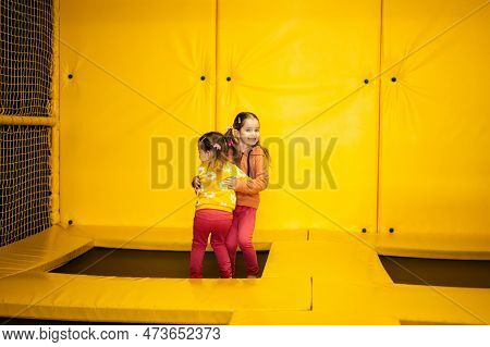 Siblings Jumping On Trampoline At Yellow Playground Park. Sisters In Motion During Active Entertaime