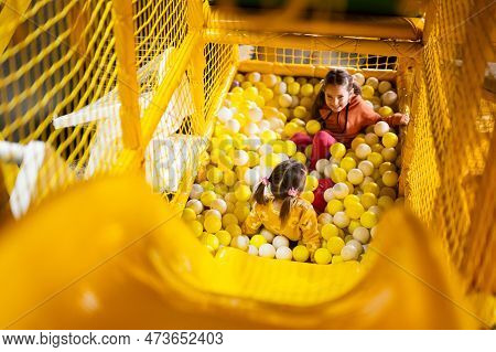 Siblings Play With Colored Balls At Yellow Playground Park. Sisters In Active Entertaiments.