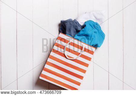 Colorful Clothing And Shopping Paper Bag On Wooden Background. Second Hand, Recycle Reuse Concept